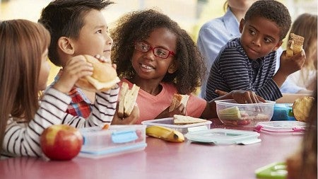 Multi-racial group of elementary-aged boys and girls eating lunch in a school cafeteria.